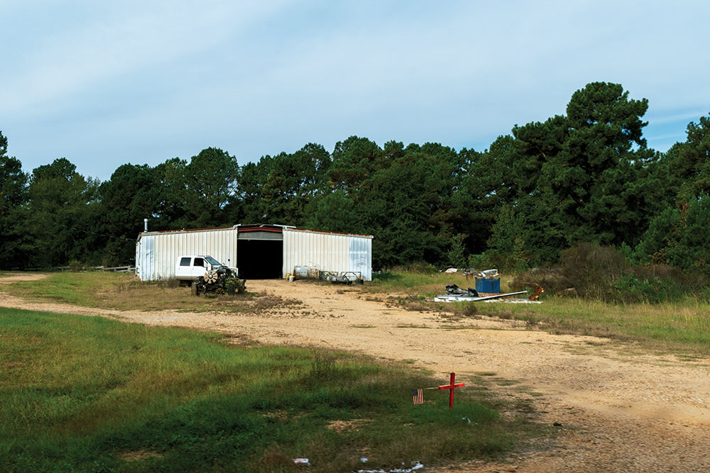 red cross with flag on it seen on right of dirt driveway in front of metal buidling