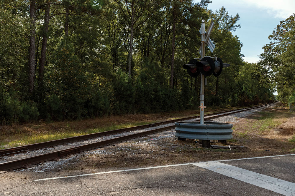 train track/road intersection - small cross seen affixed to pole of flashing light sign 