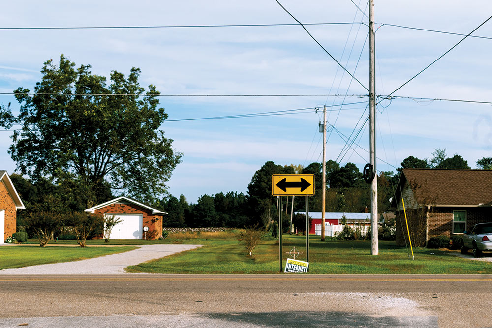 cross seen under yellow arrow sign on side of road in town