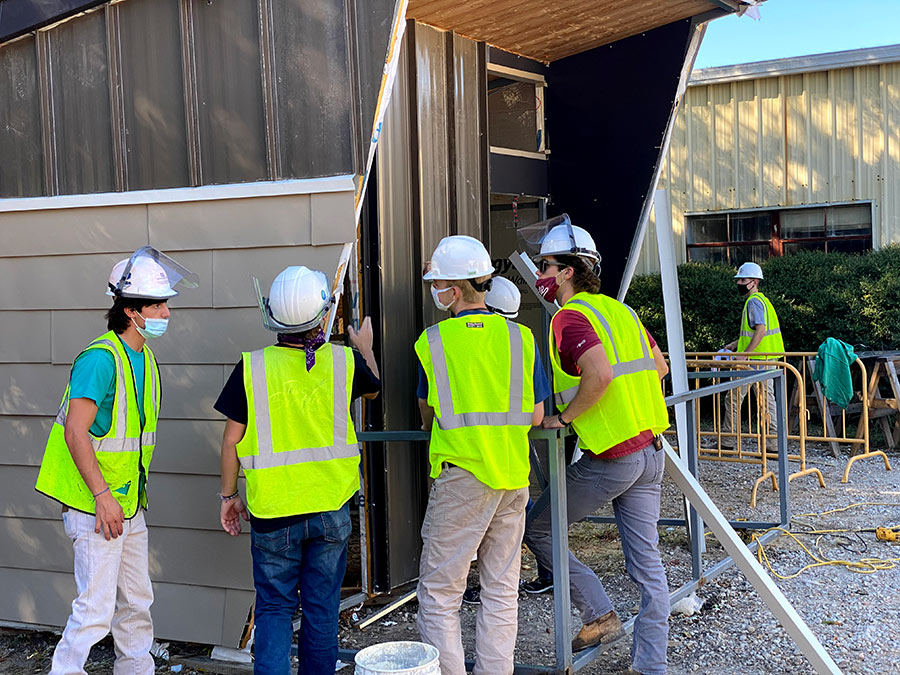 five students wearing construction PPE and masks inspect the outside of a modular building they are constructing