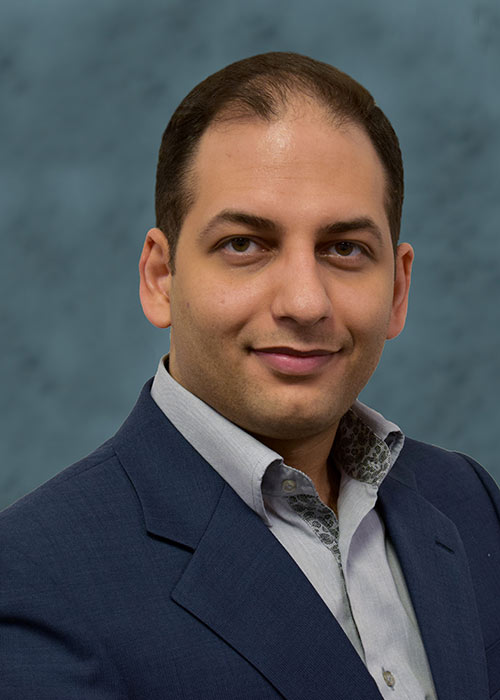 headshot Alireza Shojaei Kol Kachi wearing suit - blue/green background