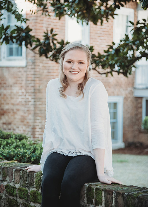 Ashley Wyatt in white sweater sits on wall in front of brick building on MSU campus