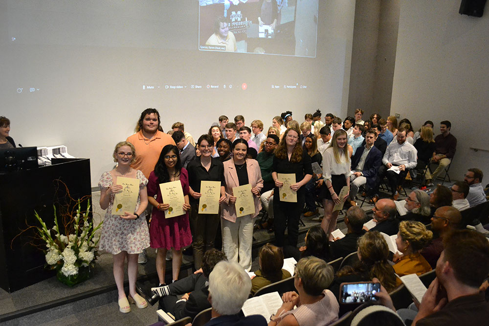 Students hold certificates on stage, posing for photo