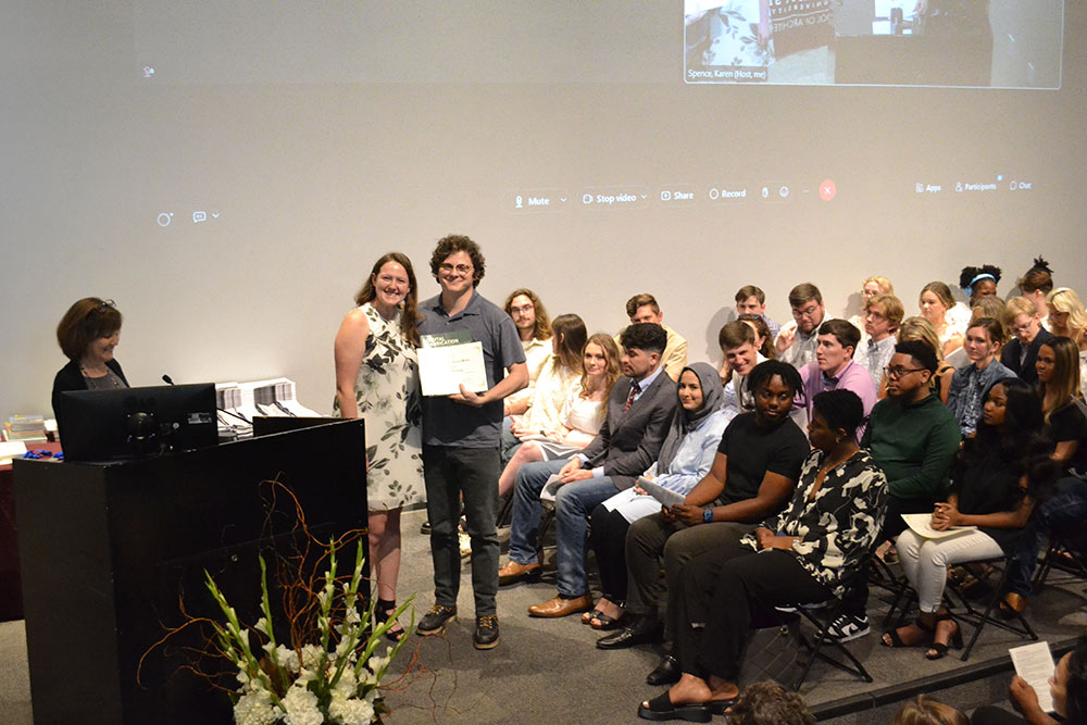 Luke Murray holds award on stage, posing for photo