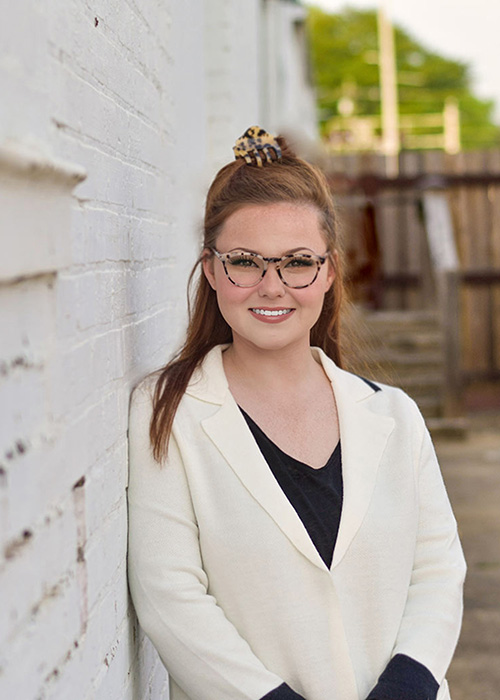 Haley Lawrence Huff leans against wall outside wearing white sweater over black shirt