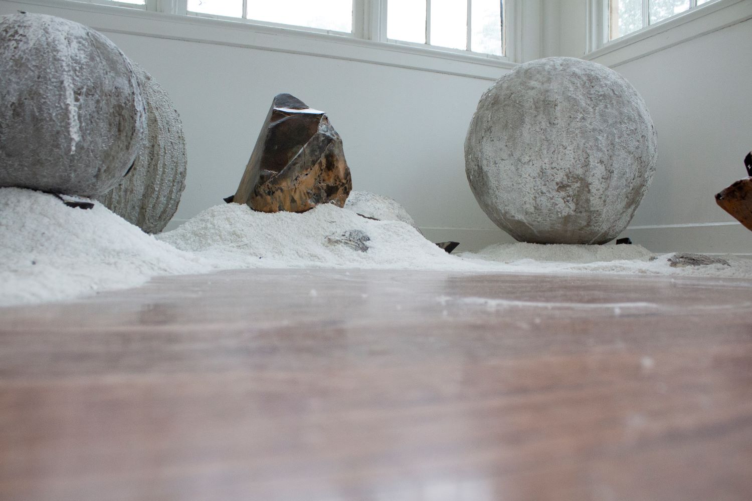 2 large concrete orbs with a large metal sculptures sitting in sand, similar to a landscape.