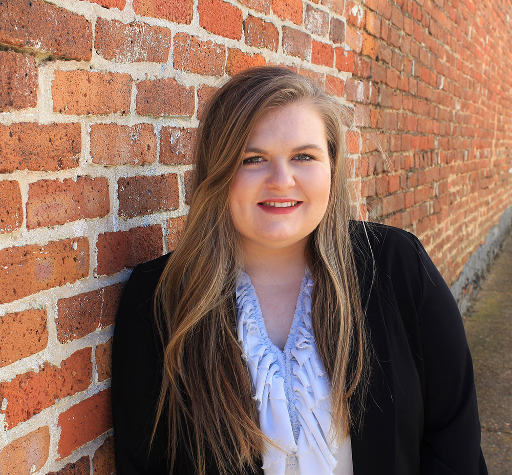 Lauren Ashley Flack leans against red brick wall