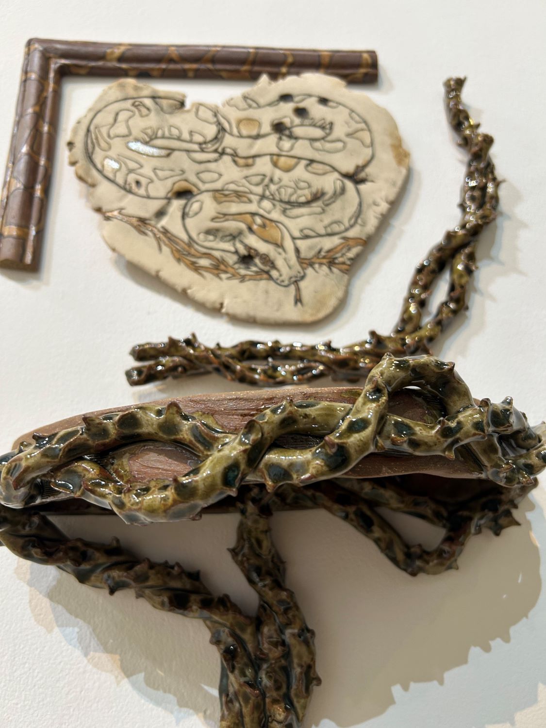 Detail shot of Python molurus bivittatus, depicting the Burmese Python on a stoneware slab surrounded by frame and shelf with thorns made with stoneware clay, glazed in Amber Celadon. 