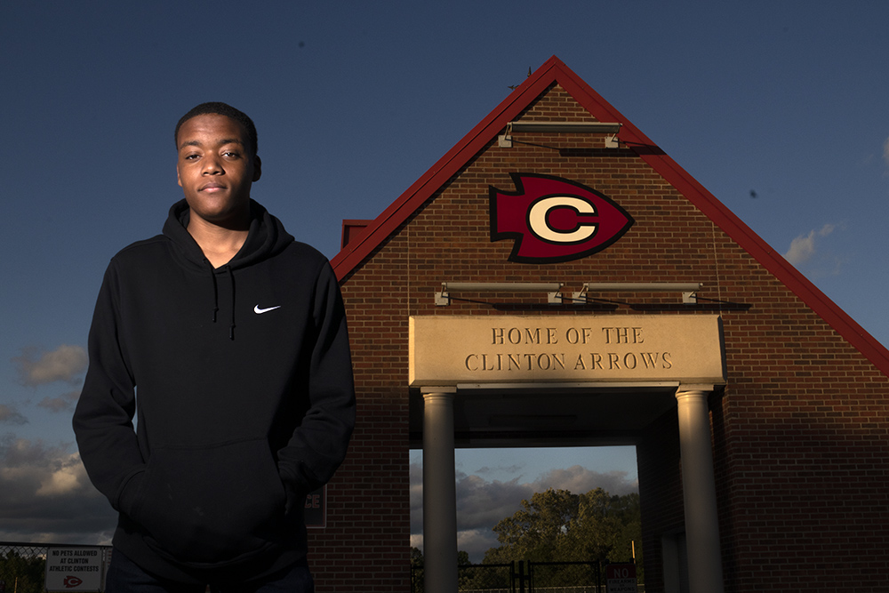 A photograph of a boy standing in front of The Clinton Arrows high school 