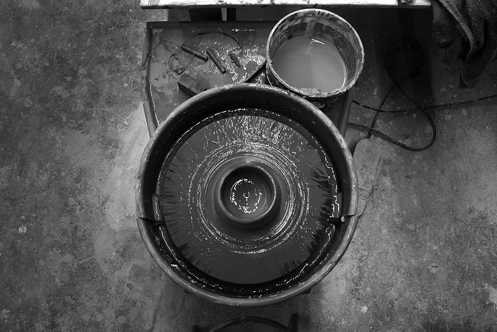 A black and white photographed image of the overhead view of a ceramic art wheel.