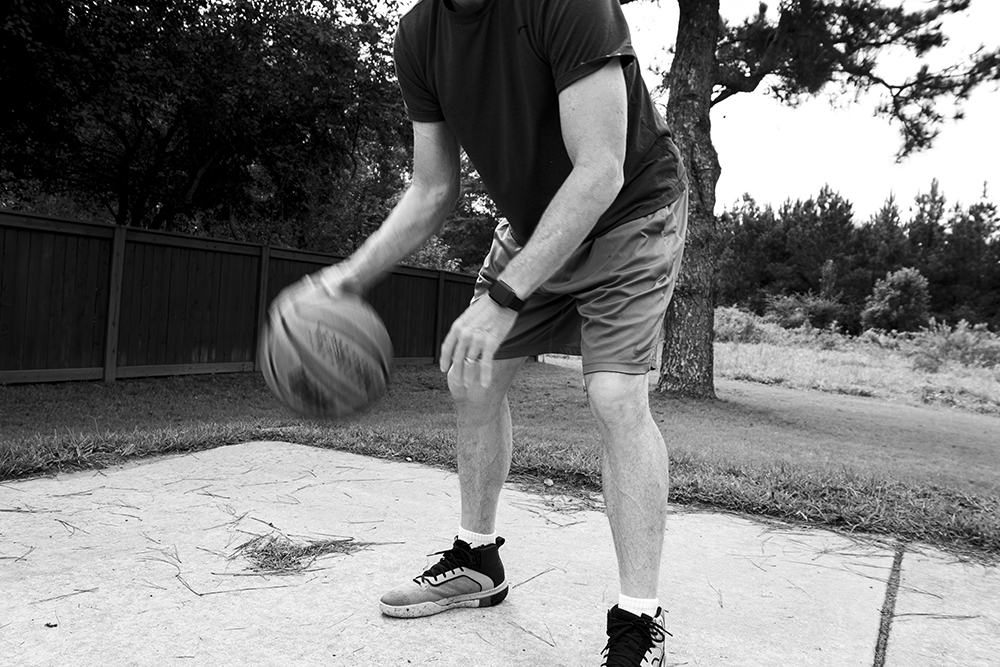 A black and white photographed image of a man dribbling a basketball.