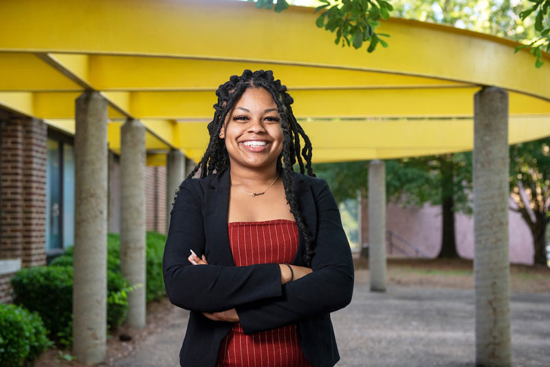 Jasmine standing with her arms crossed while smiling and wearing a red top with a black blazer.