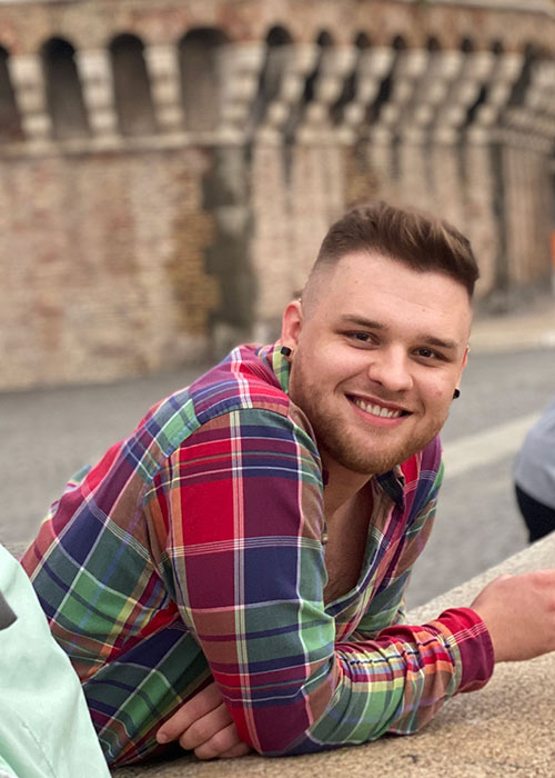 Jacob Turner in red checked shirt leans against concrete wall with concrete structure seen behind him