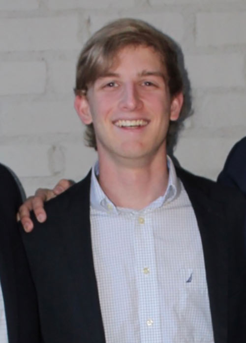 Jackson Bates poses in front of white brick wearing suit jacket