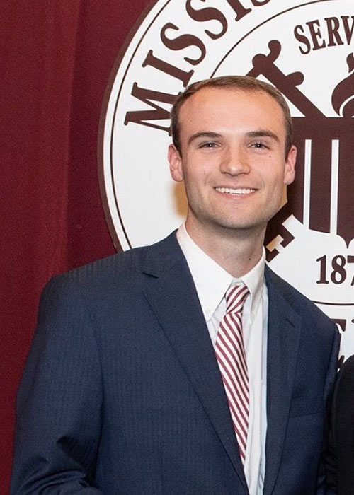 Hunter Bullock headshot - wearing suit with part of MSU seal in background