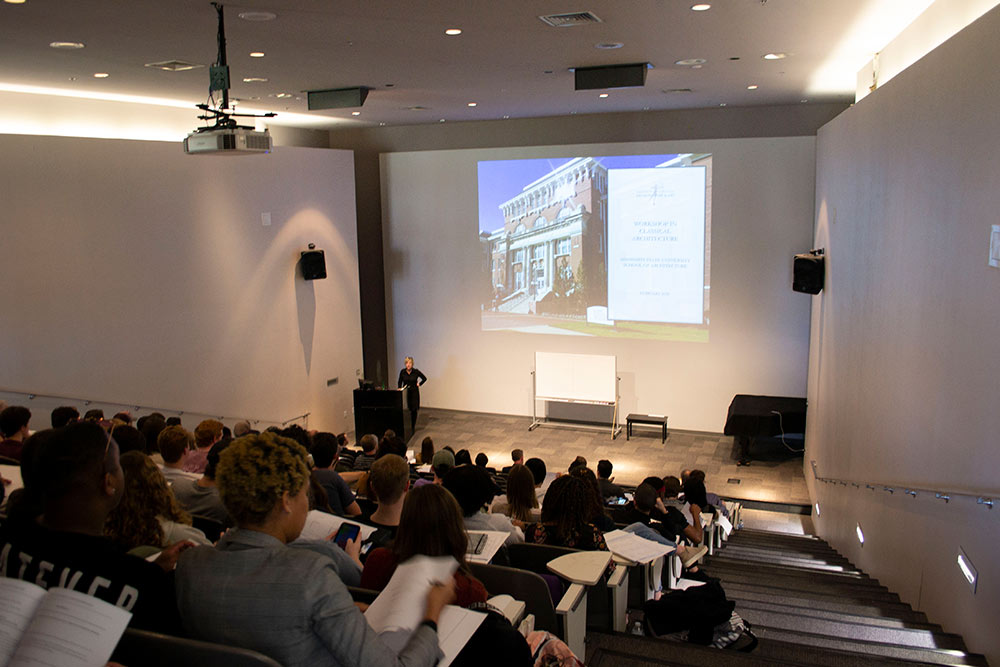 view from the back of the Robert and Freda Harrison Auditorium in Giles Hall; Kimberly Brown stands at the lectern to welcome everyone