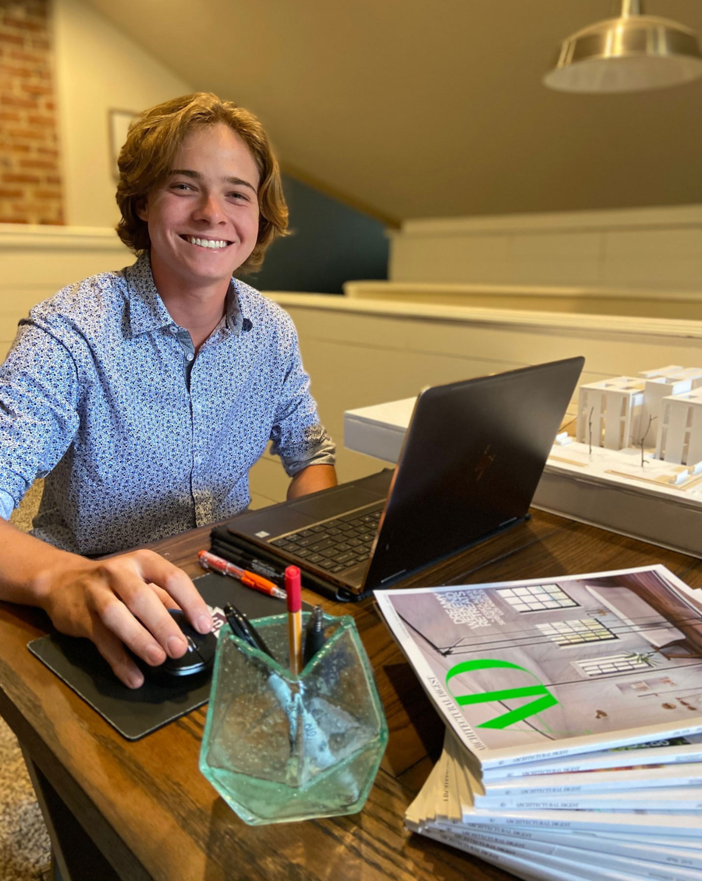 Sam Marcus sits in front of laptop at computer. architecture model on desk at his left