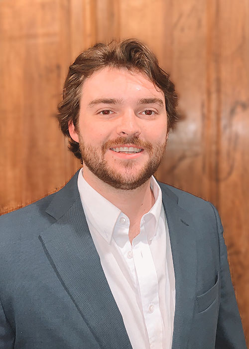 Casey Pennebaker headshot - wearing gray suit - wood background