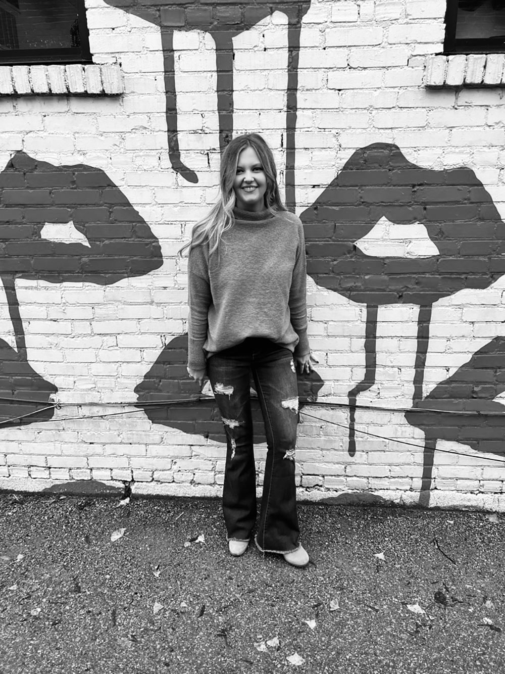 Skylynn Russell stands against painted brick wall (black and white image)