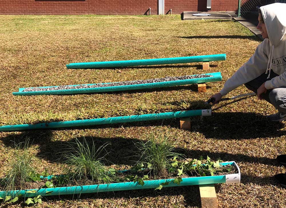 West Harrison High School student tests the varying speed of water along four 4’ runnels (green pipes) shown on grass