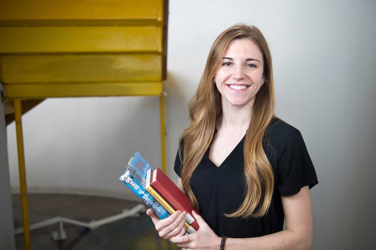 Maria Ory poses by the stairs in Giles Hall with books (Photo by Megan Bean)